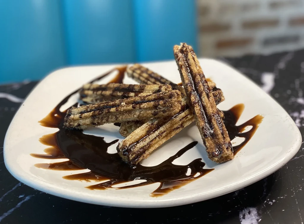 Churros with cinnamon sugar and chocolate sauce on a white plate.