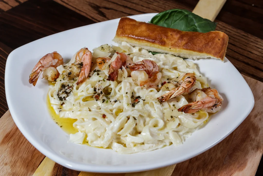 Shrimp fettuccine Alfredo with bread on a wooden board.