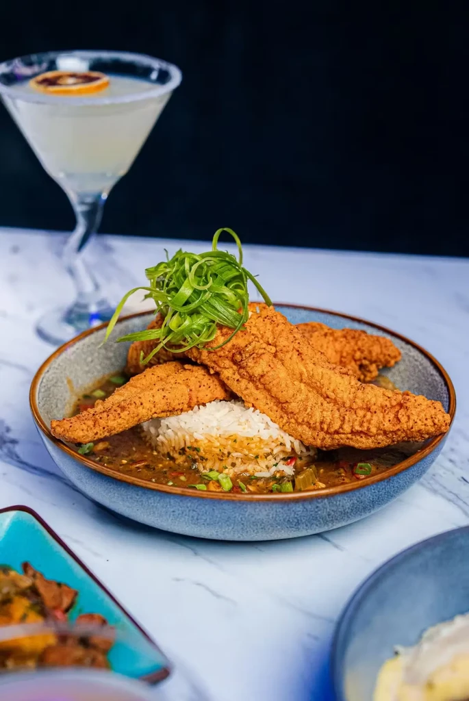 Fried fish, rice, and stew in a bowl with a cocktail.