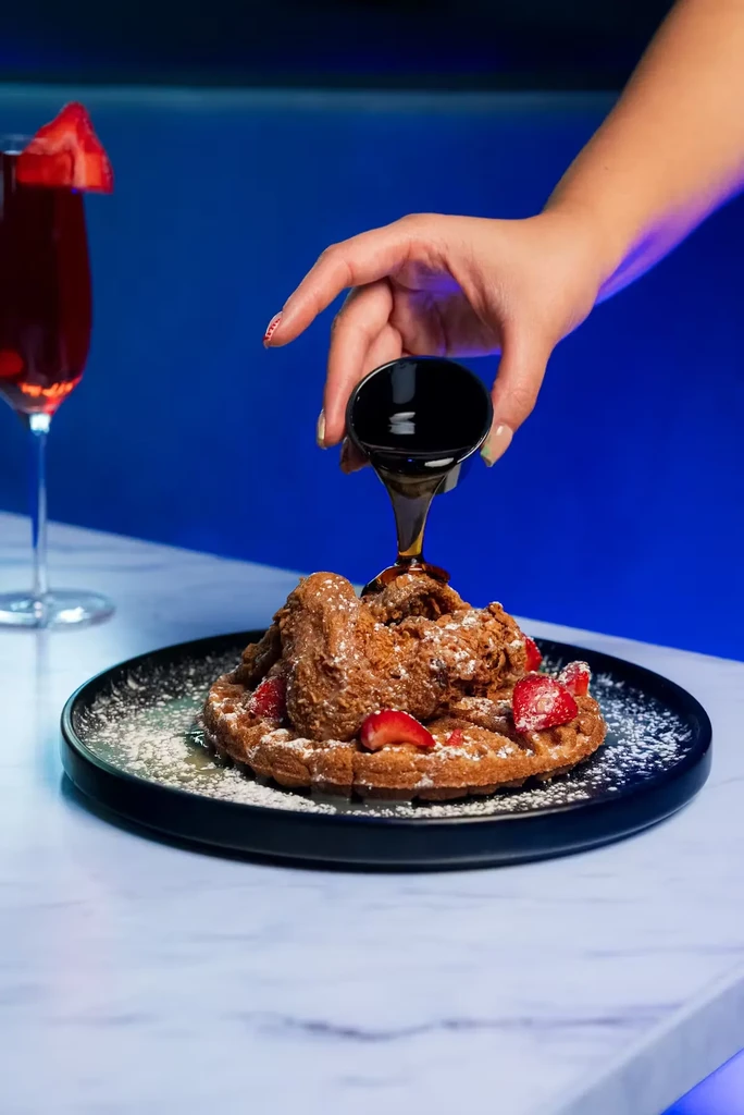 Gourmet chicken and waffles with strawberries, powdered sugar, and syrup.