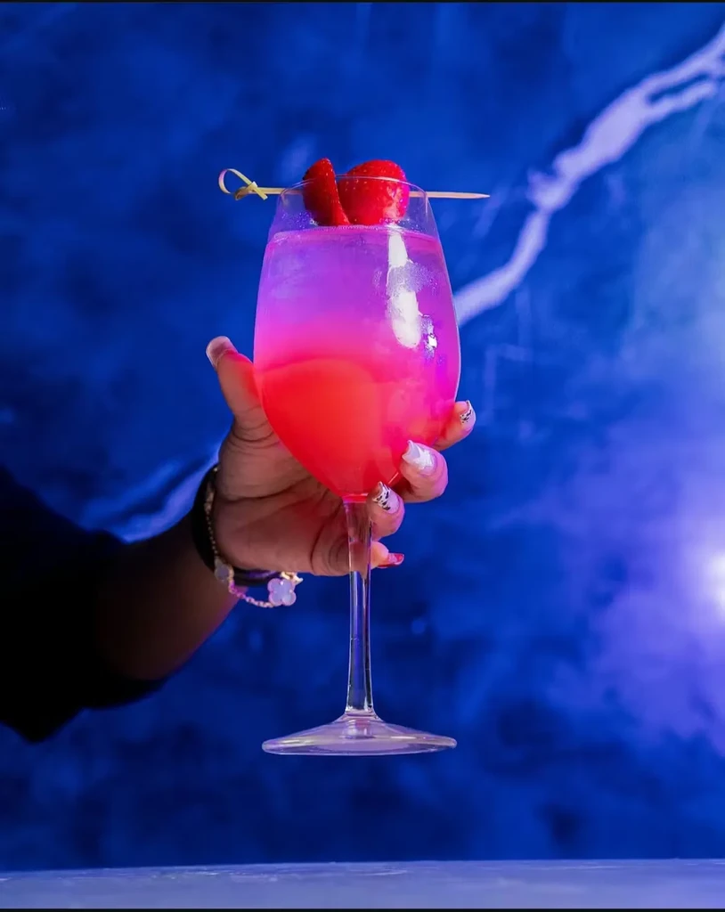 Hand holds a pink-orange cocktail garnished with strawberries.