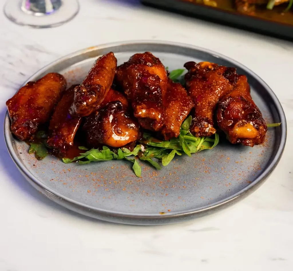 Glazed chicken wings on a grey plate with arugula.