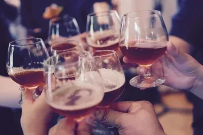 Six hands holding snifter glasses, toasting with amber beverages.