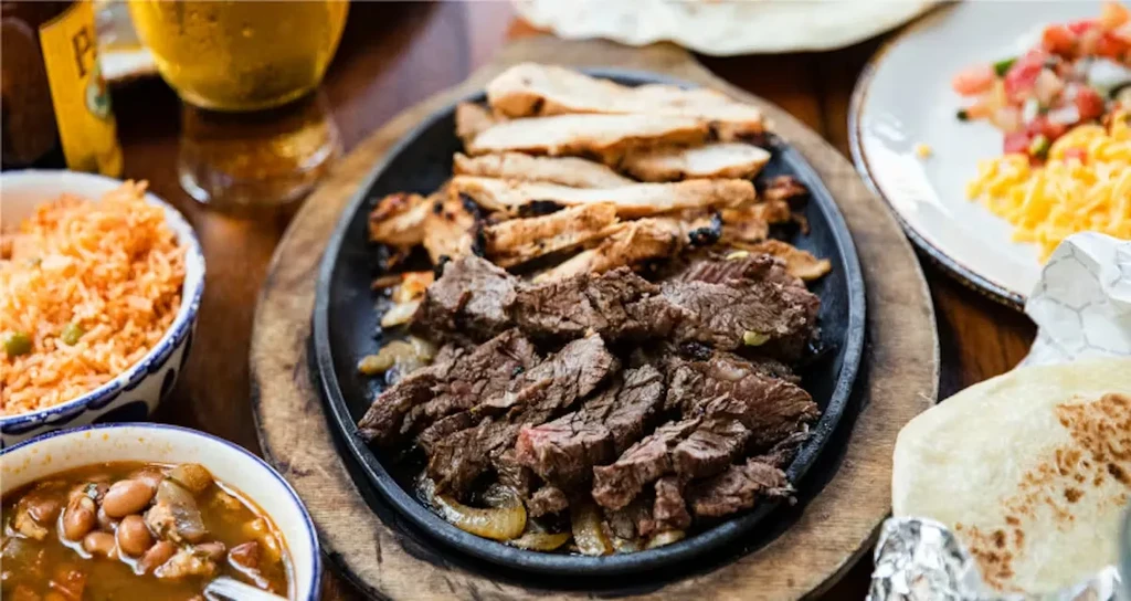 Sizzling beef and chicken fajita platter with sides on a wooden table.