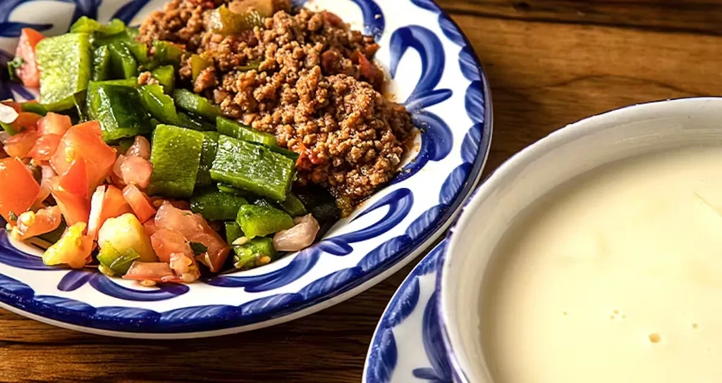 Plate of ground meat, bell peppers, tomatoes, and a side sauce.