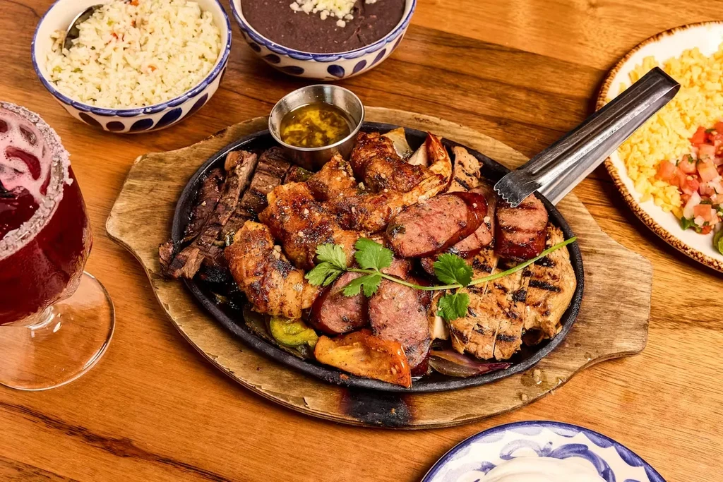 Close-up of grilled meats, rice, beans, and a red drink.