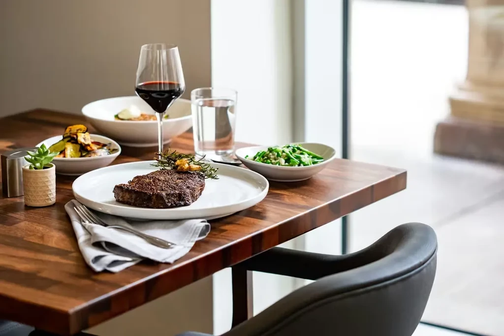 Seared steak with rosemary, side dishes, and drinks on a dark wood table.