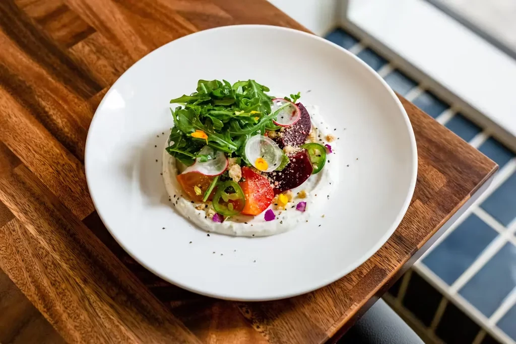 Plated appetizer with arugula, radishes, tomatoes, jalapeños, and beets.