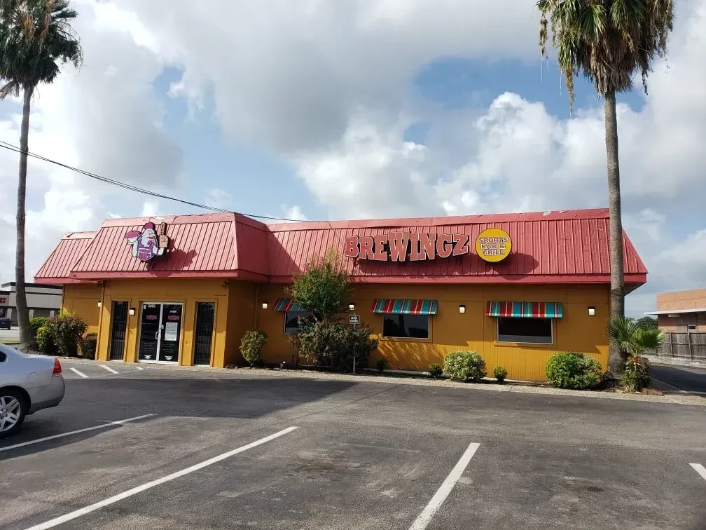 Yellow restaurant with red roof, palm trees, and clear sky.