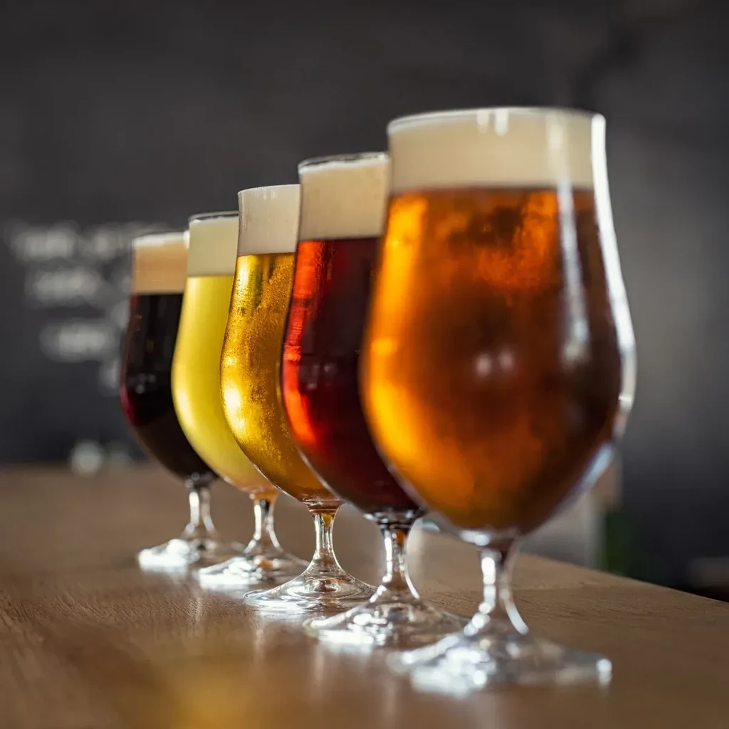 Five beer glasses, each with different colored beer, on a bar.