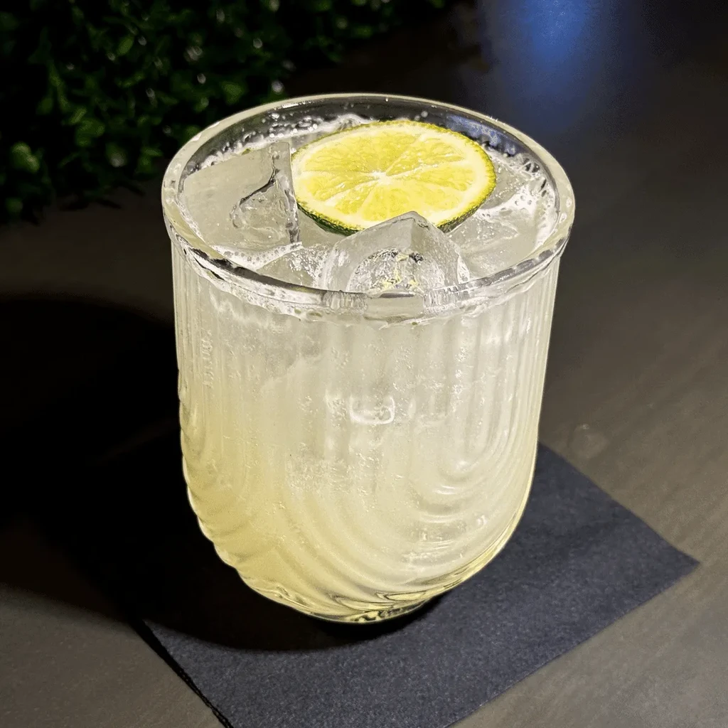 Clear drink with lime and ice in a textured glass.