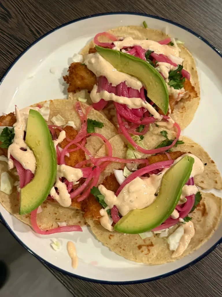 Three fish tacos on a white plate with blue rim.