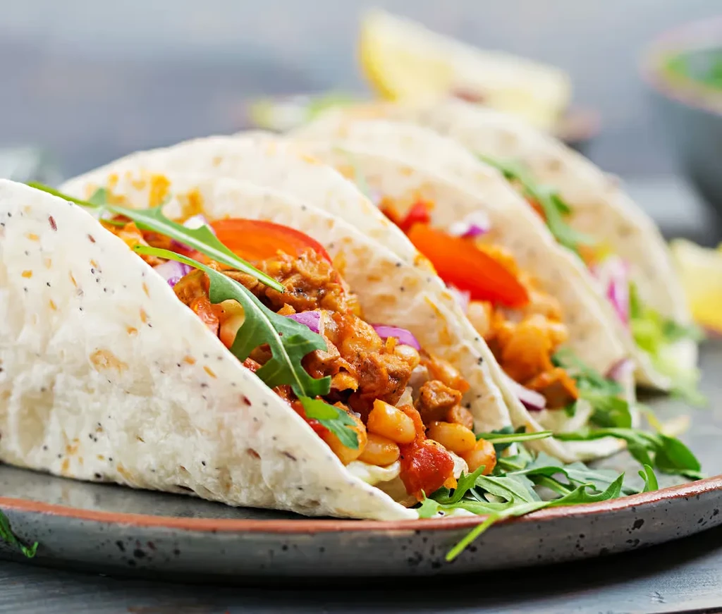 Three tacos with meat, white beans, arugula, and red onions.