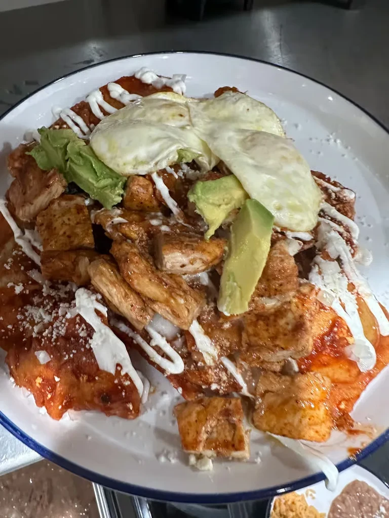 Plate of chilaquiles with chicken, avocado, fried eggs.