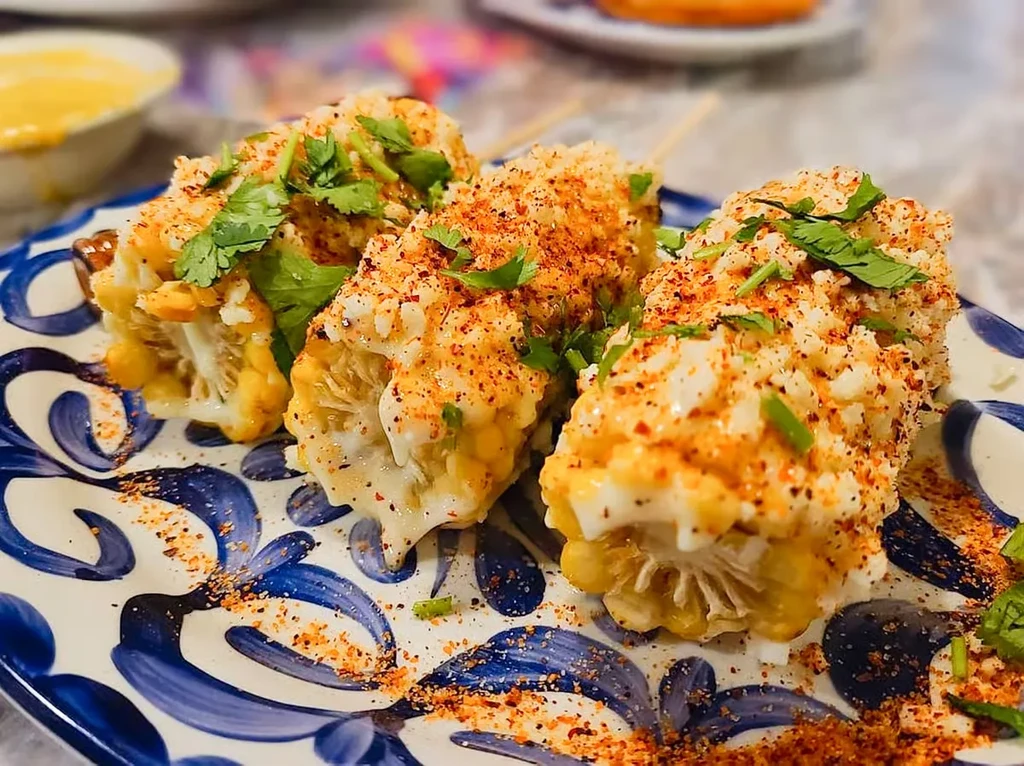 Elote: Mexican street corn with sauce, spice, and cilantro on a plate.