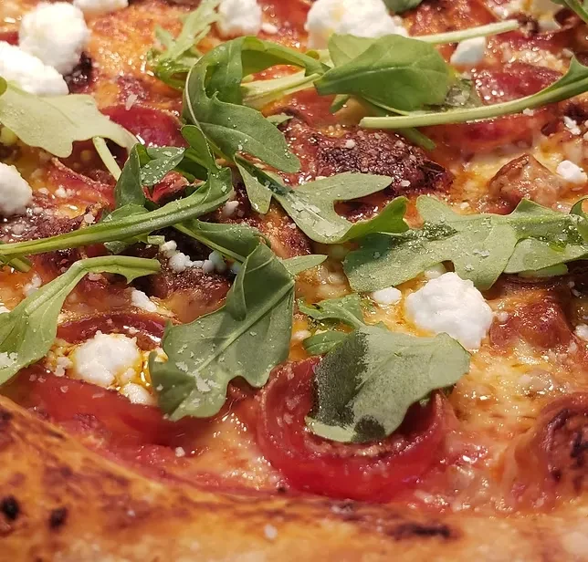 Close-up, high-angle shot of pizza with tomatoes, arugula, and cheese.
