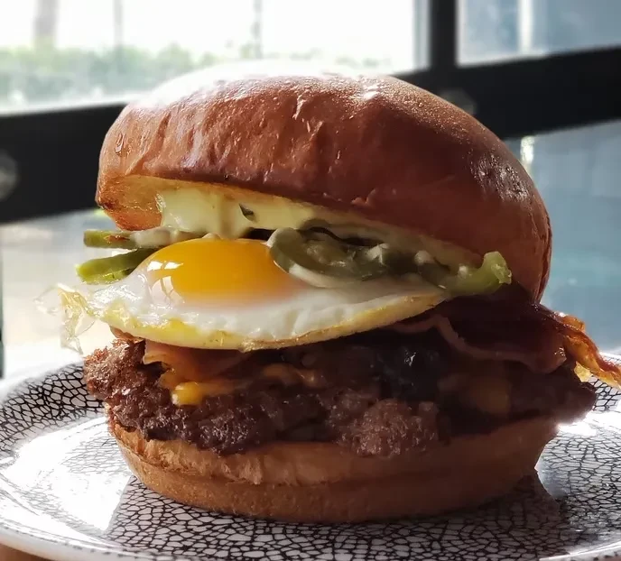 Gourmet burger with egg, bacon, cheese, and jalapeños on patterned plate.