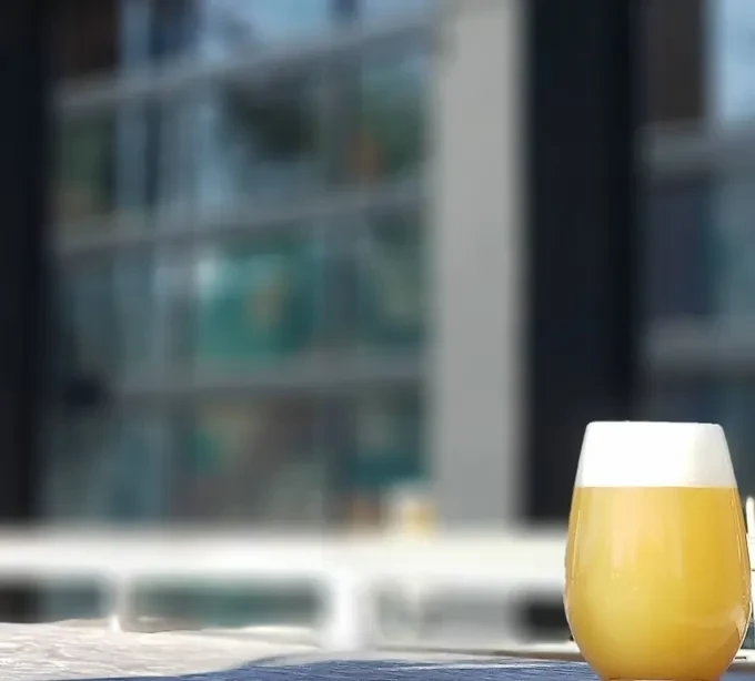 Glass of yellow-orange beverage with a white foam head.