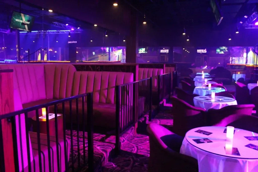 Dimly lit bar interior with purple and pink neon lighting.