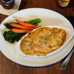 Creamy baked dish with a golden crust, carrots, and green vegetables.