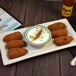Six golden-brown croquettes or fritters around a dip on a white platter.