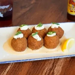 Six fried appetizers with sauce and garnish on a white plate.