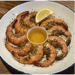 Cooked shrimp with dipping sauce and lemon wedge on a plate.