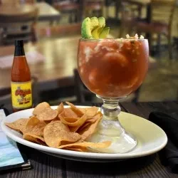 Goblet glass of red cocktail with avocado, tortilla chips.