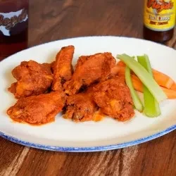 Plate of chicken wings, celery, and carrots on a wooden table.