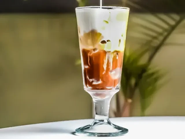 Layered iced drink with dark orange and white liquids being poured.