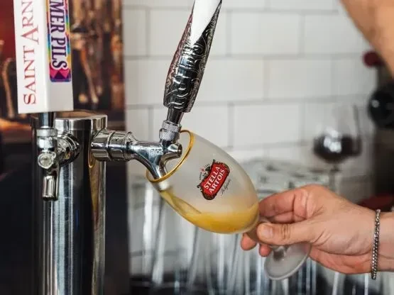 Hand holding a Stella Artois glass, beer pouring from a tap.