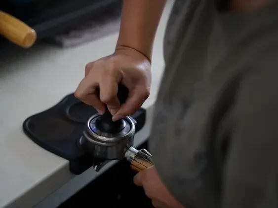 Hands pressing coffee grounds into a portafilter with a tamper.