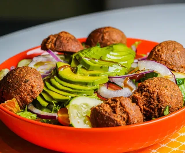 Vibrant salad with falafel, avocado, red onion, and cucumber.