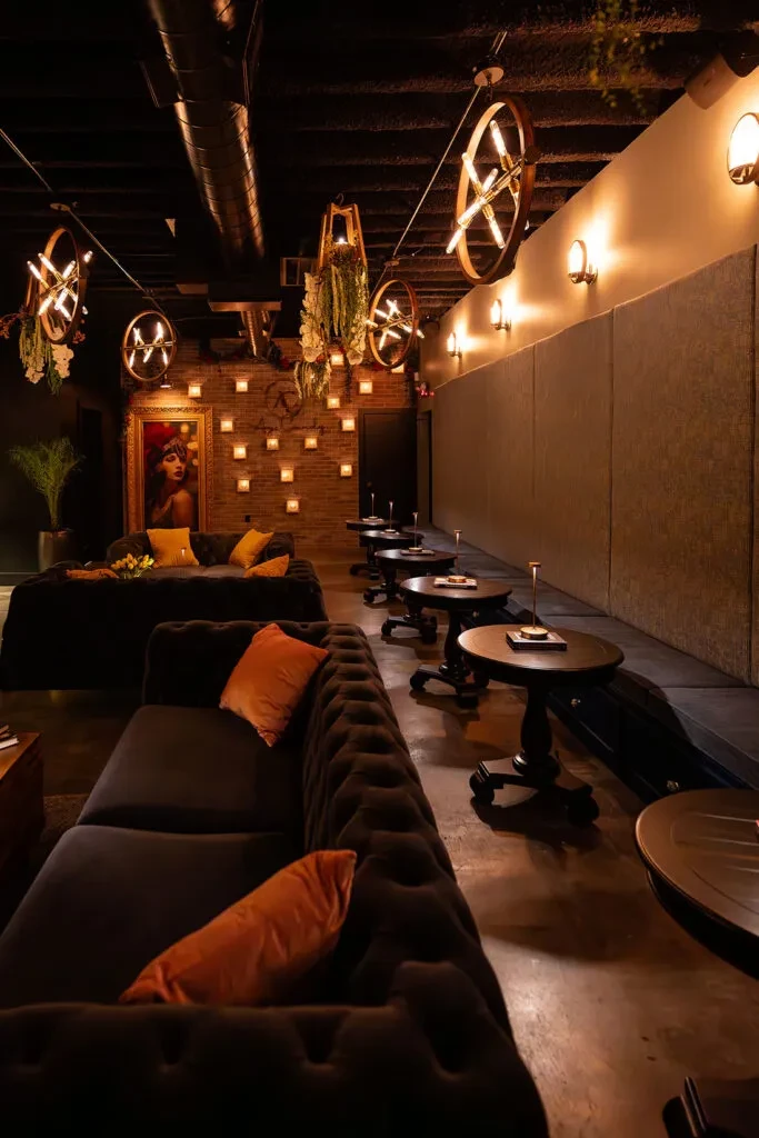 Dimly lit, upscale bar lounge with velvet couches and ornate tables.
