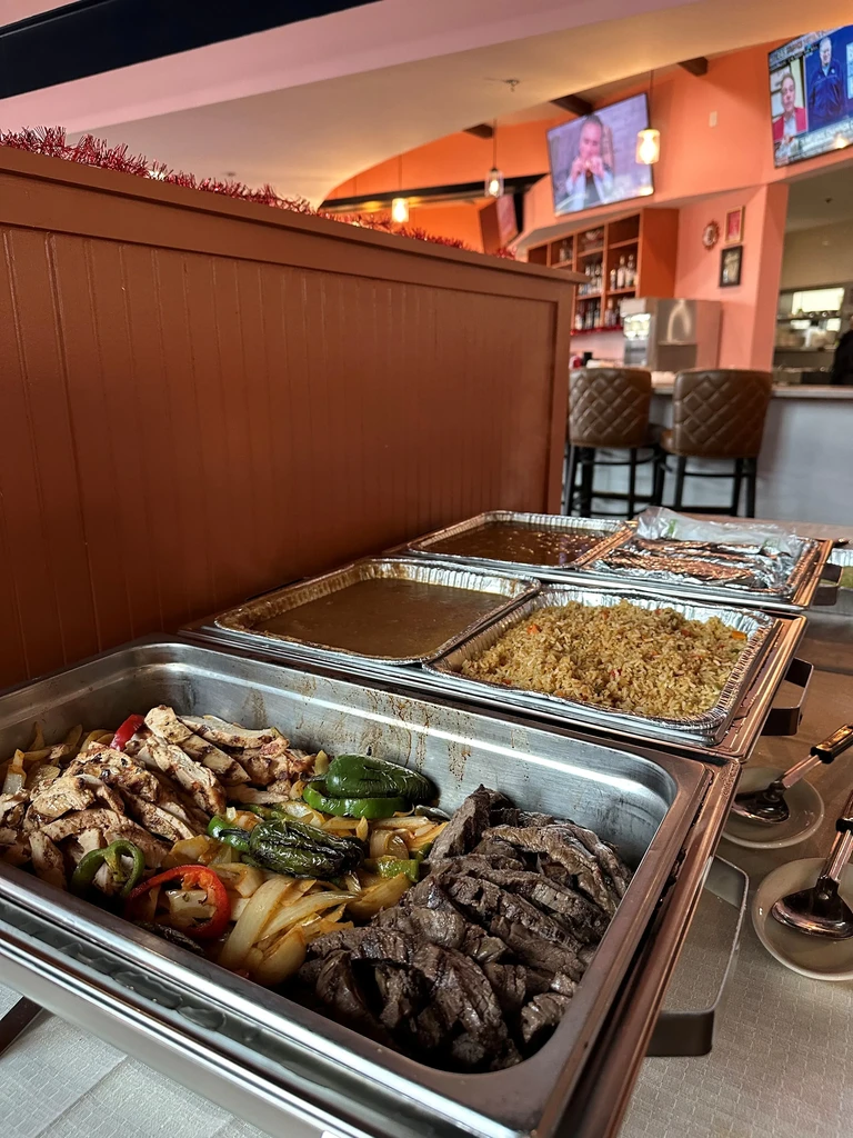 Buffet chafing dishes with grilled chicken, steak, peppers, and rice.
