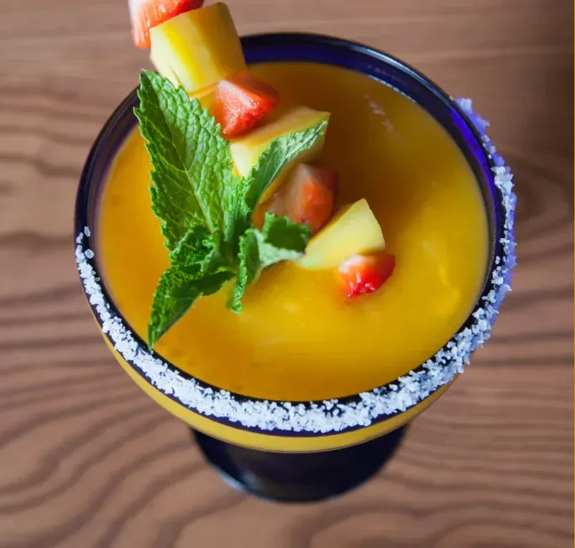 Overhead view of a yellow-orange drink garnished with fruit and mint.