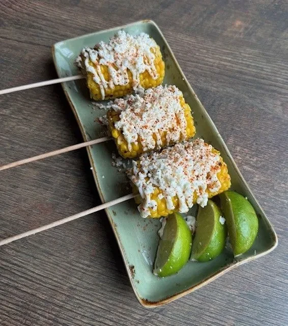 Three pieces of elote, or street corn, on a light green plate.