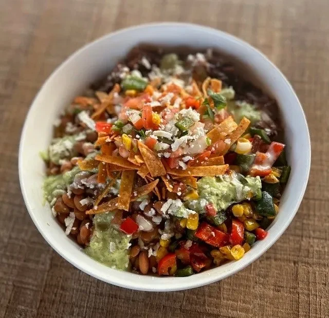 Overhead shot of a colorful food bowl with beans, vegetables, and sauce.
