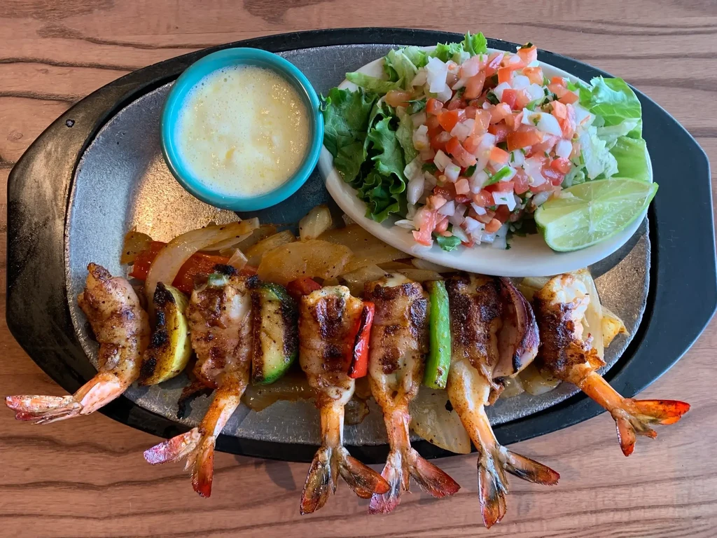 Shrimp fajitas with salad and sauce on a wooden table.