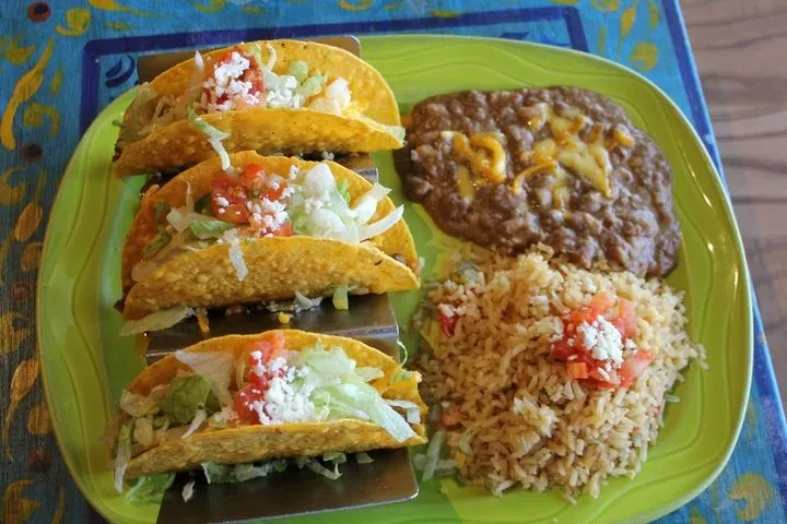 Three hard-shell tacos, refried beans, and Mexican rice on a plate.