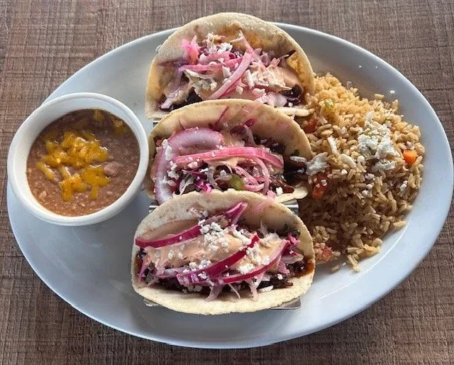 Three tacos, refried beans, and rice on a white plate.