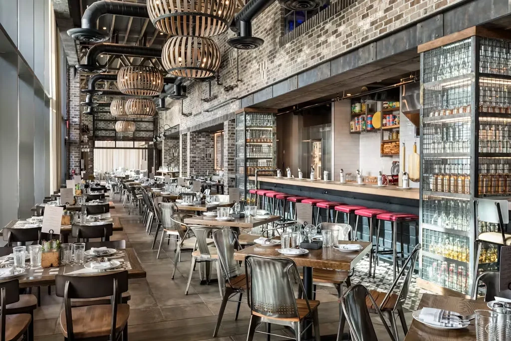 Modern restaurant interior with wooden tables, red-cushioned bar stools, and exposed brick.