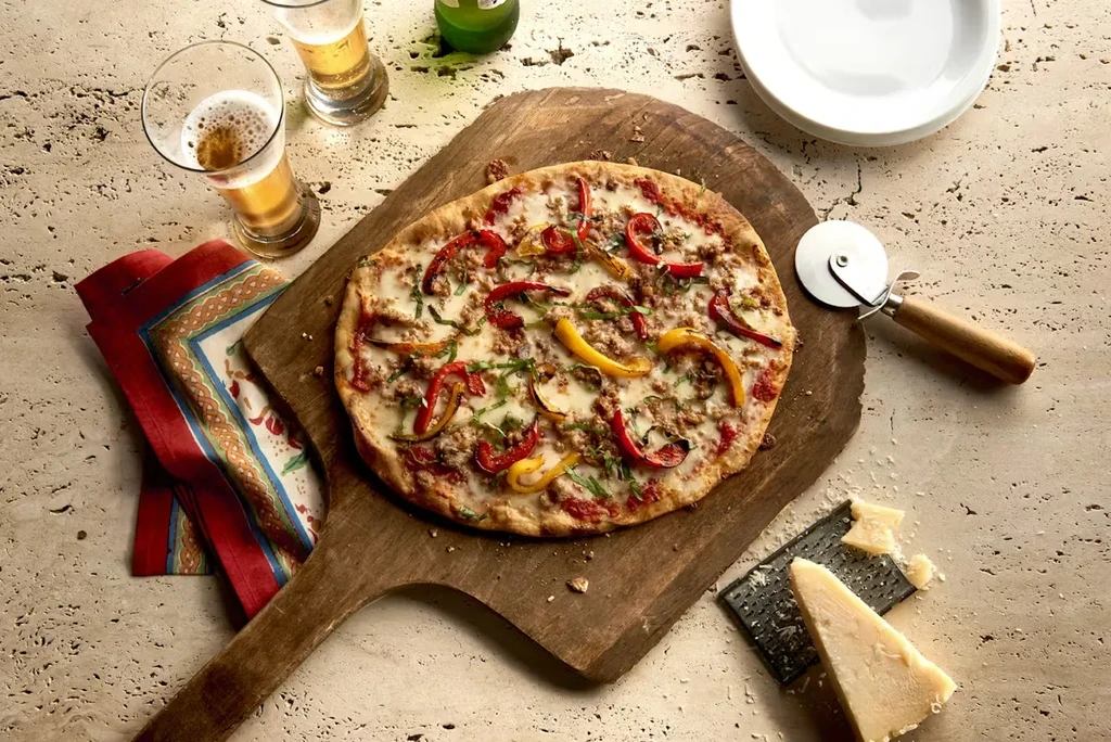 Overhead view of a pizza, beer, and cheese on a stone surface.