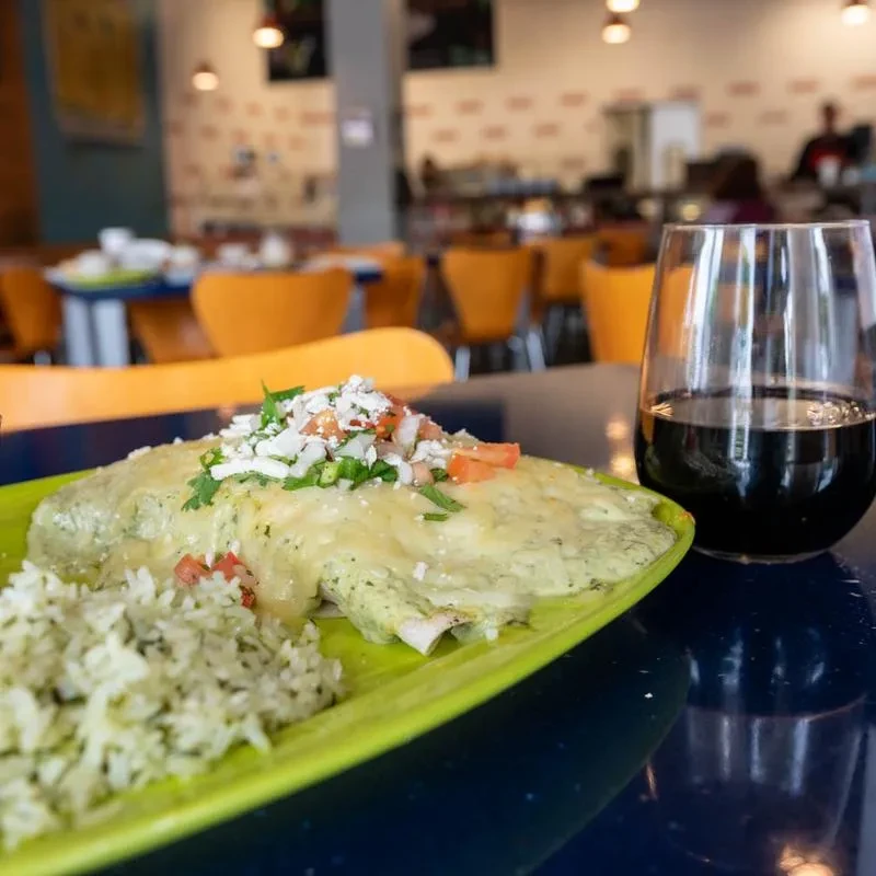 Enchiladas with green sauce, rice, and a dark drink on a blue table.