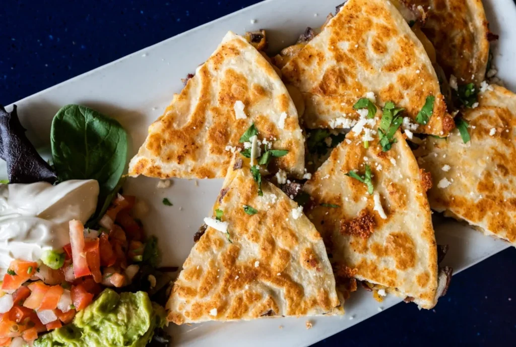 Quesadilla pieces topped with cheese and cilantro, with three condiments.