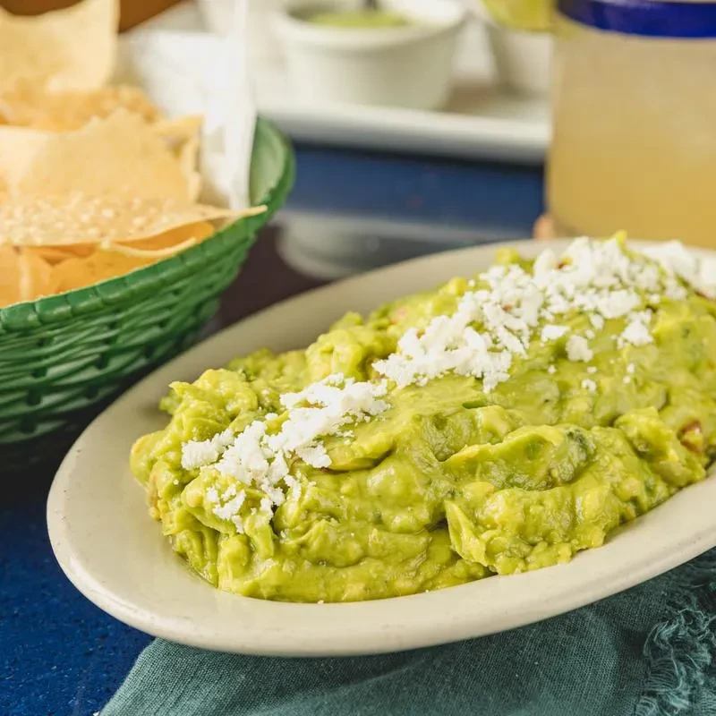 Guacamole topped with crumbled cheese, tortilla chips, and a drink.