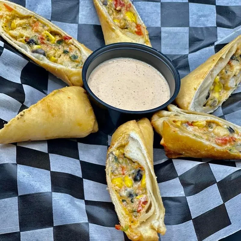 Fried egg rolls with corn and pepper filling around a dipping sauce.