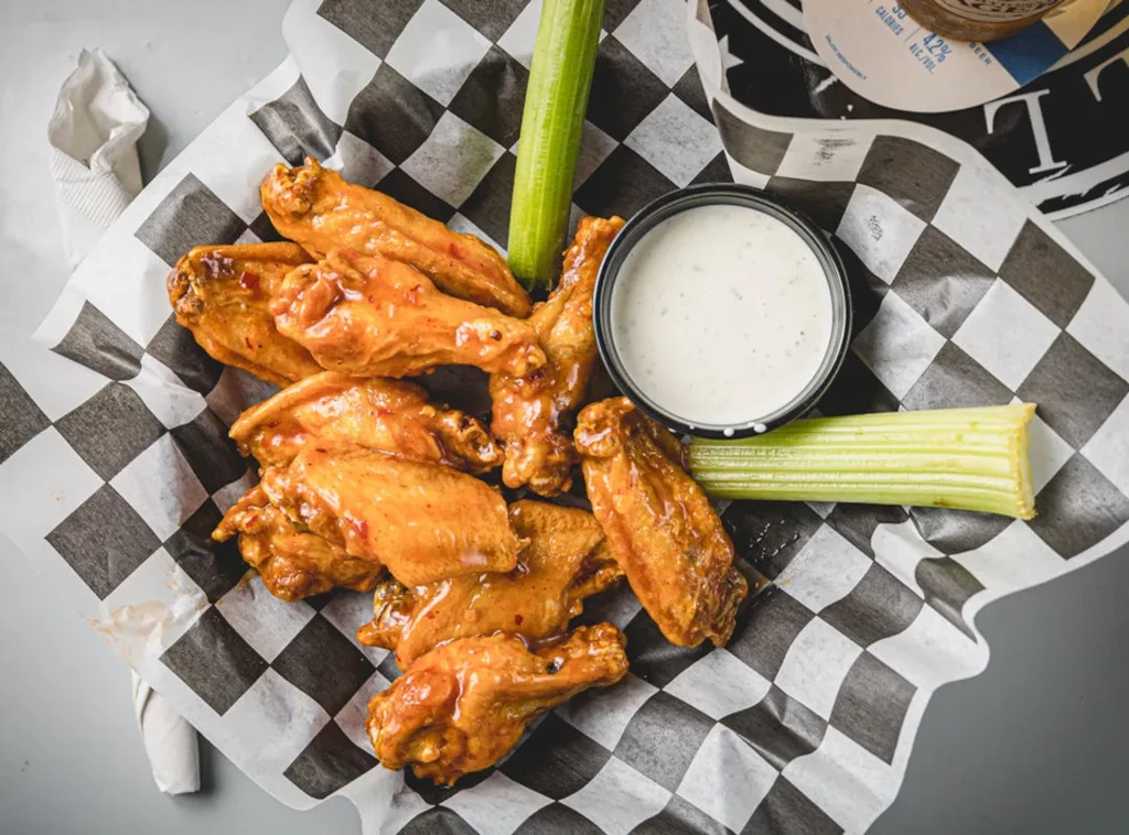 Top-down view of buffalo wings in a basket with celery and dip.