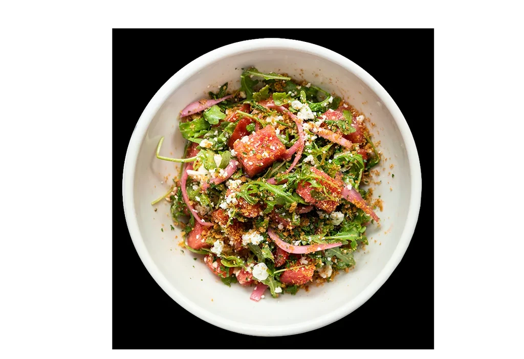 Overhead view of a colorful salad with watermelon, feta, and greens.
