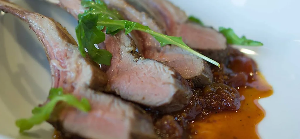 Gourmet medium-rare lamb chops with sauce and greens on a white plate.